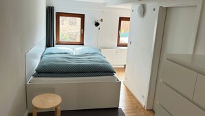 Una camera da letto con un letto, uno sgabello di legno, un termosifone e due finestre.
