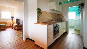 A modern kitchen with wooden flooring, white cabinetry, and a built-in oven. - NEW Apartment Blumenstraße in Korbach (Korbach)