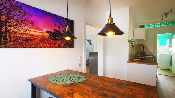 A modern kitchen with a wooden countertop, pendant lights, and a vibrant sunset painting on the wall. - NEW Apartment Blumenstraße in Korbach (Korbach)