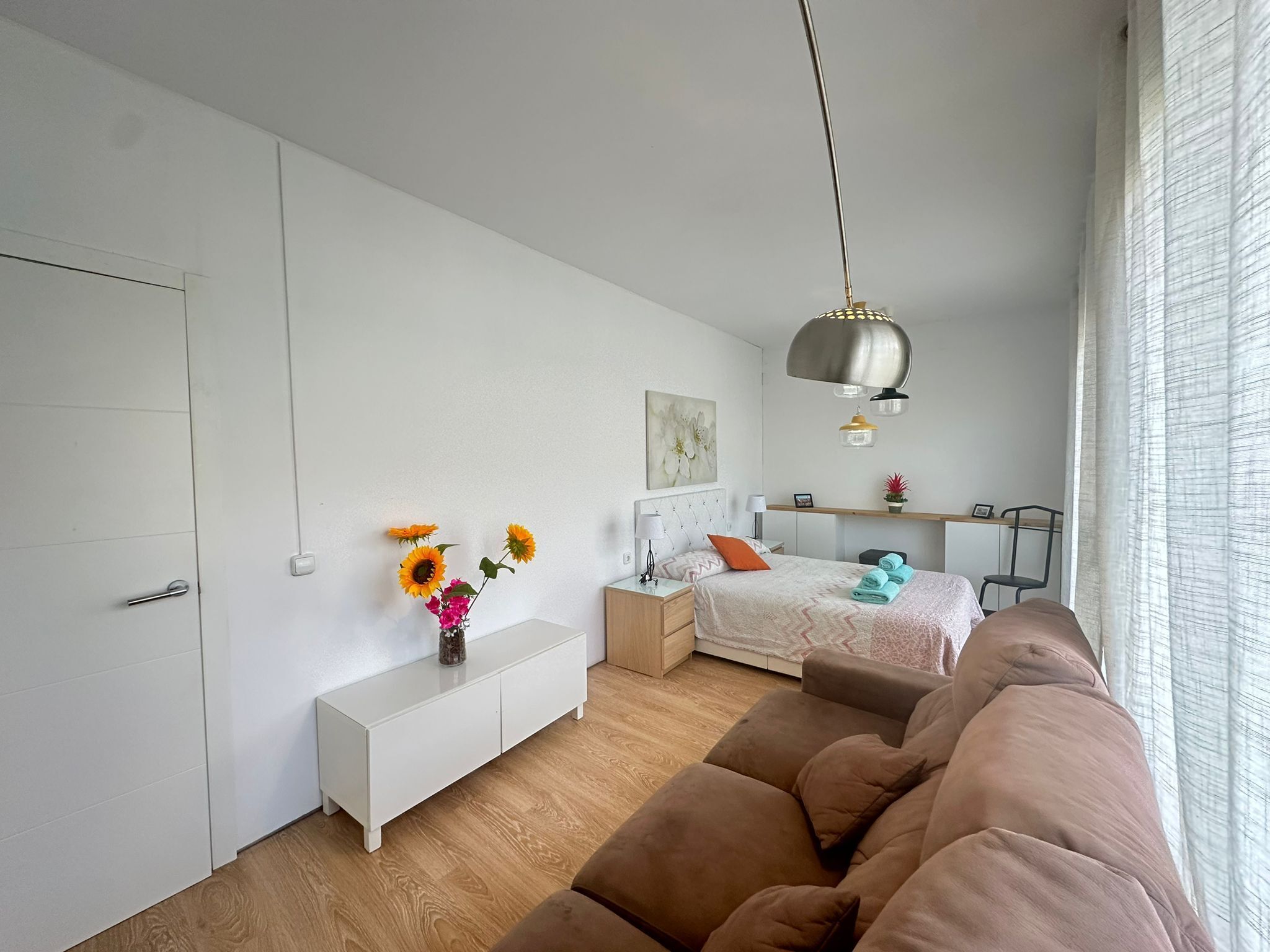 Een moderne slaapkamer met een bed, nachtkastjes, een bankje, een hanglamp en een raam met gordijnen.