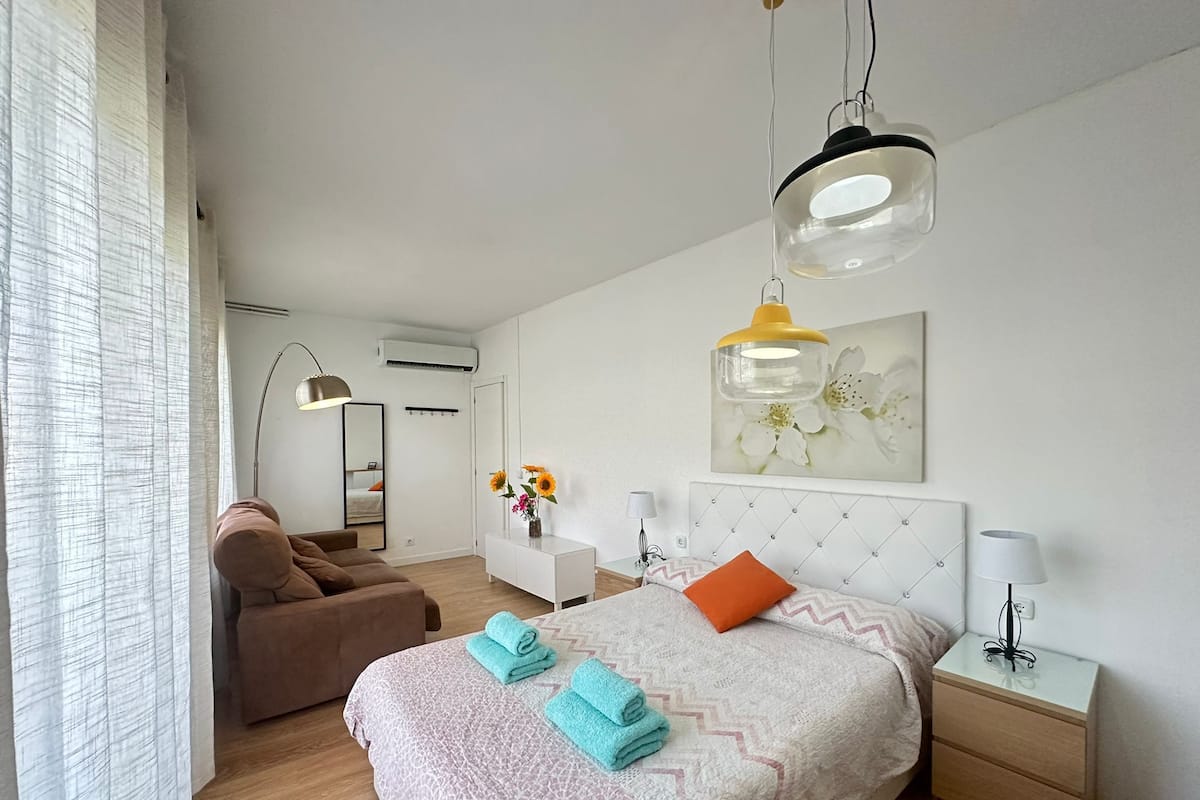 Un dormitorio moderno con una cama grande, un sillón marrón, un aparador blanco y un espejo.