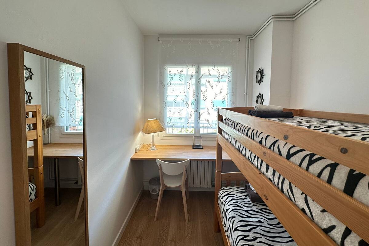 Habitación tipo dormitorio con literas, un escritorio, una silla, una lámpara y una ventana con cortinas.
