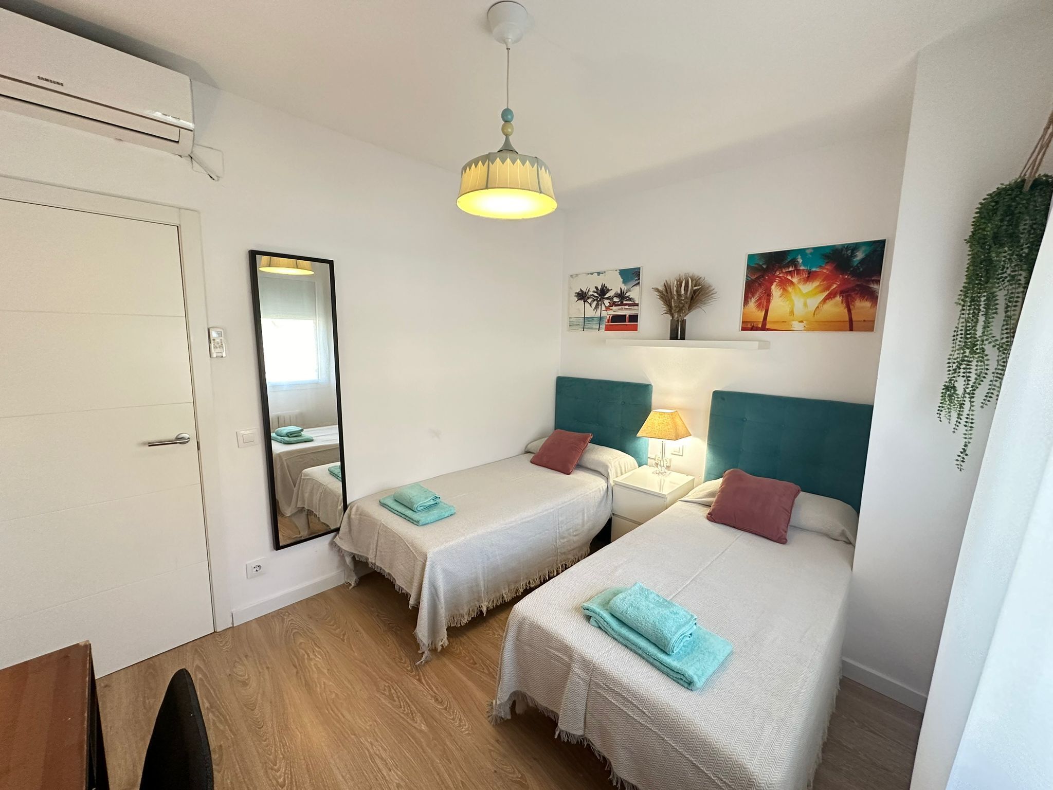 Een hotelkamer met twee bedden, een spiegel, een plafondventilator en een wandlamp.