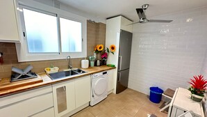 A modern kitchen with a built-in dishwasher, a sink, and a refrigerator. There is a window above the sink and a ceiling fan. - Rooms Borrell (Barcelona)