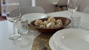 Una mesa de comedor dispuesta con platos blancos, dos copas de vino, un cuenco de adornos y un mantel individual texturizado.