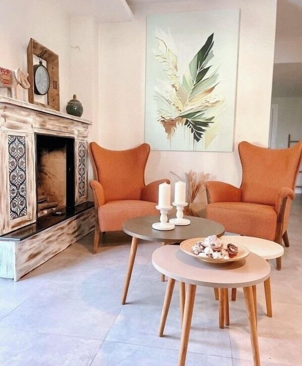 A living room with a fireplace, two orange armchairs, a round coffee table, and a large abstract painting on the wall. - The One Alacati (Cesme)