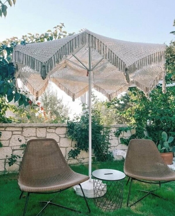 Een terras met twee rieten stoelen en een ronde tafel, onder een grote geweven parasol.