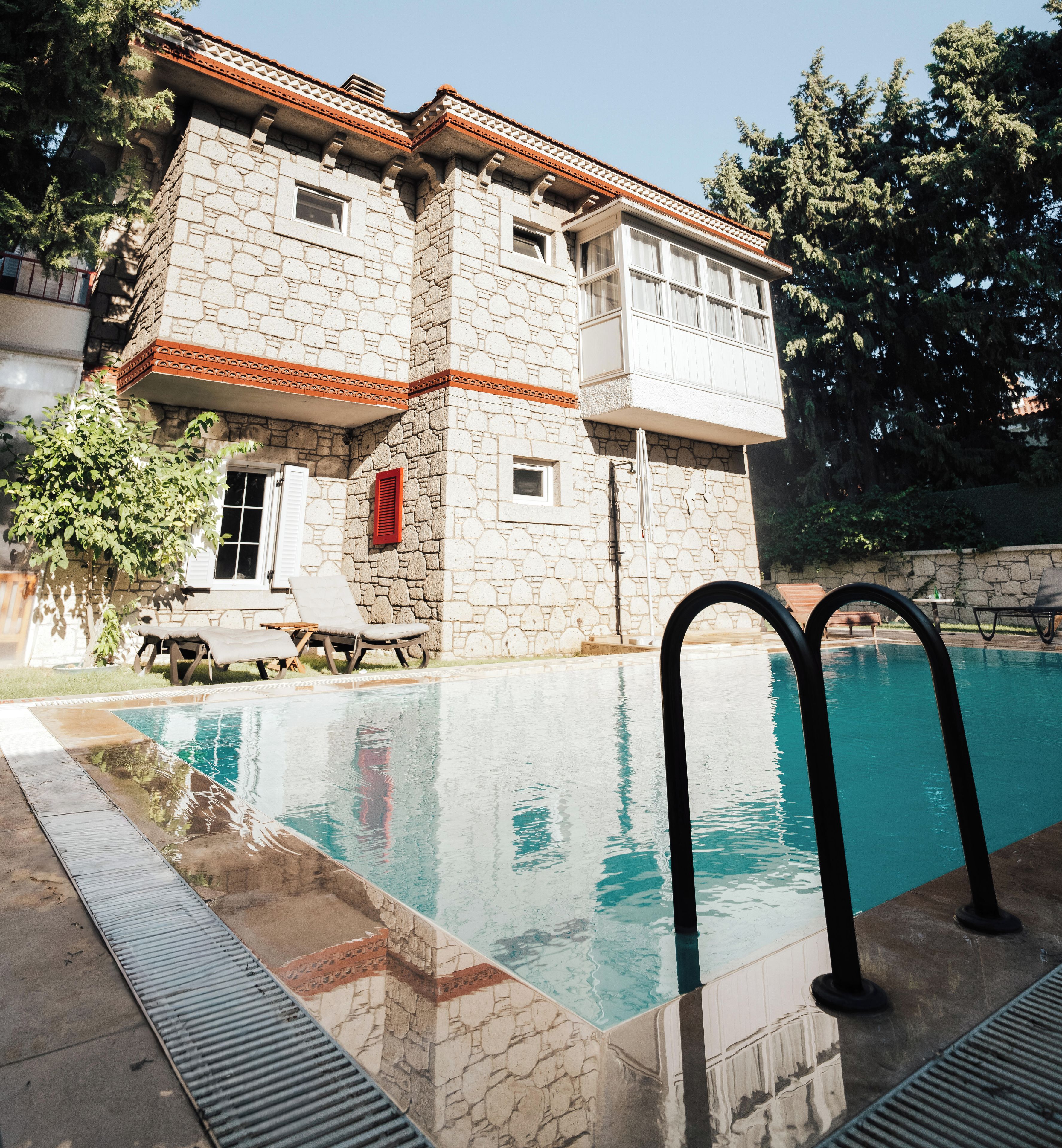 Un edificio de piedra con piscina, un persiano rojo y un cielo azul despejado.