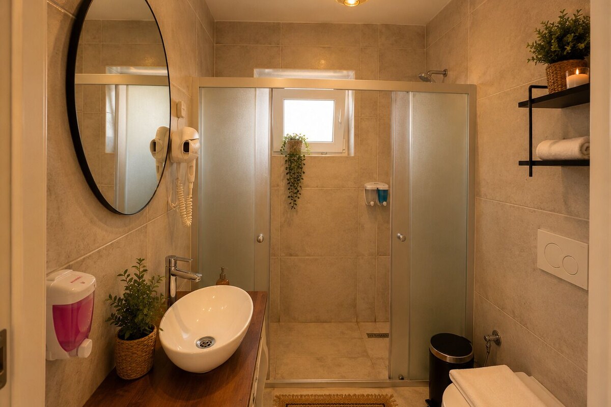 Ein modernes Badezimmer mit einem großen, ovalen Waschbecken, einem Spiegel, einem Handtrockner, einer Duschkabine und einer Toilette.