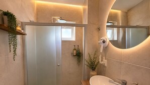 Ein modernes Badezimmer mit Duschabtrennung aus Glas, einem Holzwaschtisch, einem großen Spiegel und einem Wäschekorb.