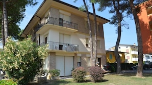 A multi-story residential building with balconies, surrounded by trees and a well-maintained lawn. - Charming family vacation home (Bibione)