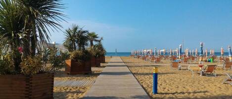 Une plage avec une promenade en bois menant à la mer, bordée de palmiers et de chaises de plage.