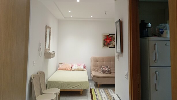 A small, well-lit bedroom with a bed, a sofa, and a refrigerator. - VIP Tunisia  (Halq al Wadi)