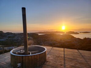 A hot tub on a wooden deck with a view of a sunset over a mountainous landscape. - Panoramautsikt over kyst og skjærgård (Vestland)
