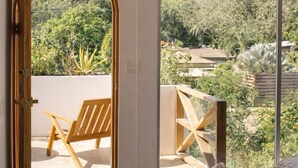 An open doorway leading to a balcony with a wooden chair and a white pouf.