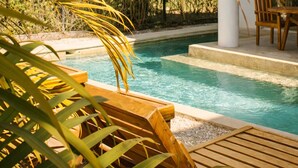 A pool area with a wooden deck, a covered seating area, and lush greenery.