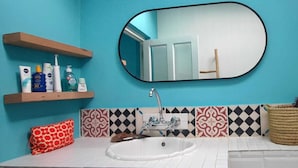 A bathroom with a white sink, a mirror, and a shelf with toiletries. - Beautiful Appartement With Balcony and Great View at Bokaap (Cape Town)