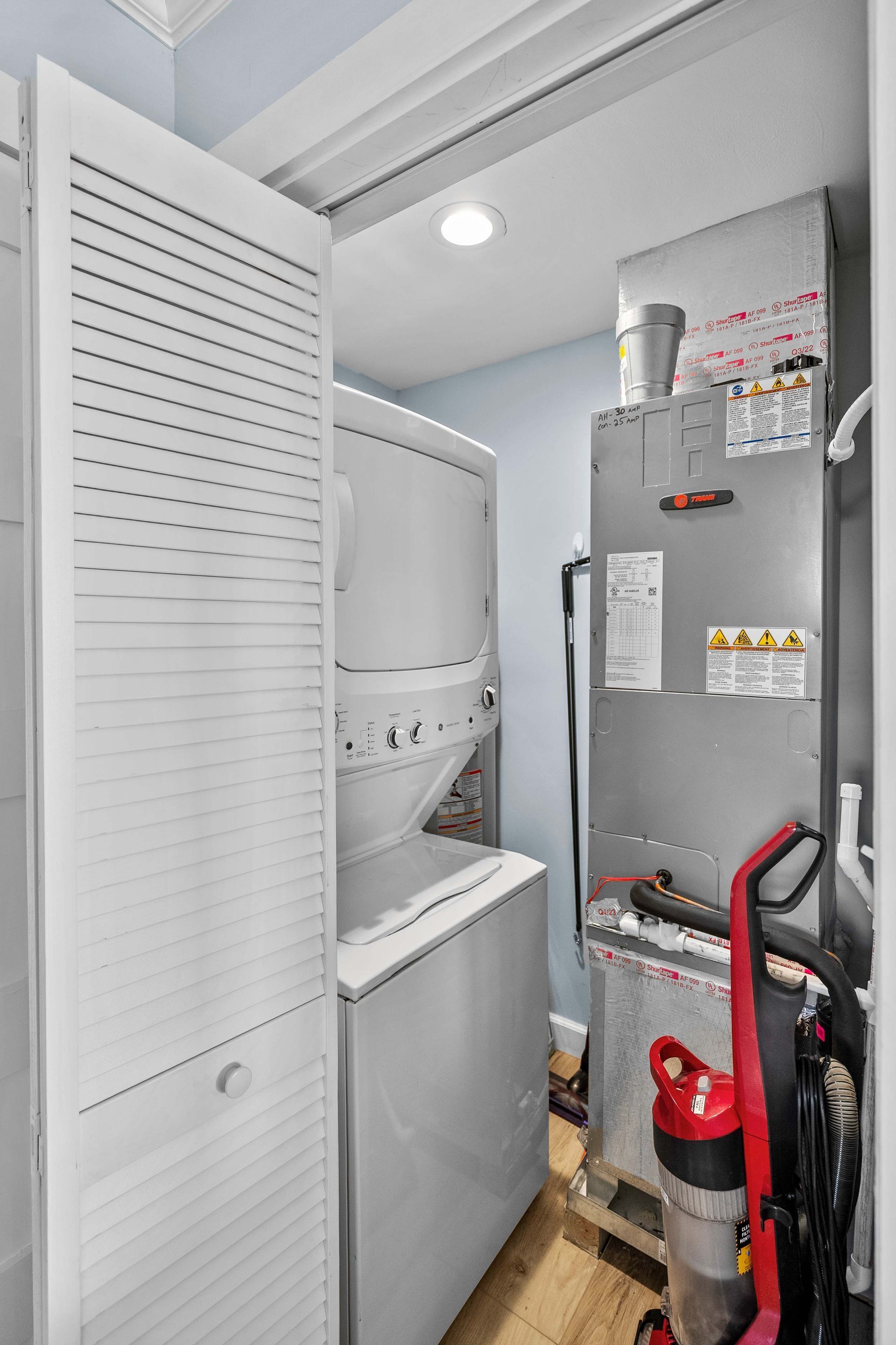 A compact laundry room with a washing machine, dryer, and a utility cart with a red gas cylinder.
