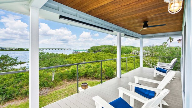 A covered outdoor deck with white lounge chairs and a view of a bridge over water. - Sunset Sights Waterfront BBQ Fire Pit Dolphins (St. Augustine)
