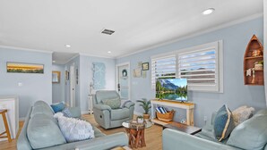 A living room with a light blue sofa, a wooden coffee table, and a television. - Sunset Sights Waterfront BBQ Fire Pit Dolphins (St. Augustine)