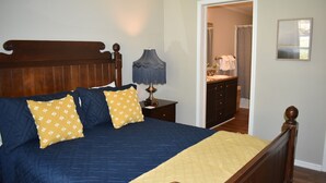 A bedroom with a wooden bed, a nightstand with a lamp, and a bathroom visible through an open door. - Waterfront LKN Hideaway Relax & Recharge (Troutman)
