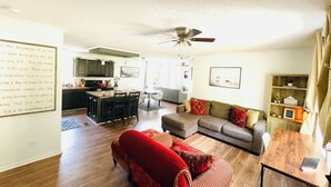 A spacious living room with a red sofa, a grey couch, and a wooden coffee table. There is a kitchen in the background with dark cabinets and a ceiling fan. - Waterfront LKN Hideaway Relax & Recharge (Troutman)