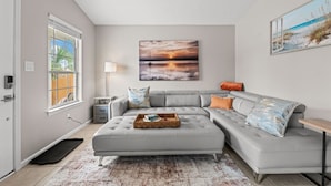 A modern living room with a grey sectional sofa, a side table, and a large painting of a sunset.