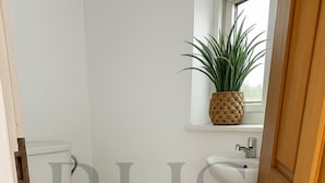 A bathroom with a toilet, sink, and a window with a plant. - 4-bed Home in Maidenhead (Maidenhead)