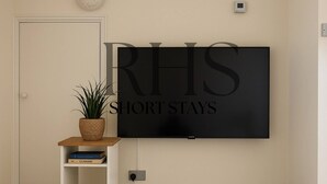 A flat-screen TV mounted on a wall with the text "RHS SHORT STAYS" above it. - 4-bed Home in Maidenhead (Maidenhead)