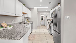 Una cocina moderna con gabinetes blancos, encimeras de granito, electrodomésticos de acero inoxidable y piso de baldosas.