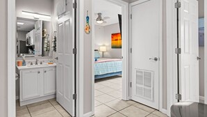 Pasillo que conduce a un baño con lavamanos, espejo y toallero blancos.