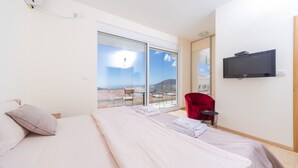 Habitación de hotel con cama, televisor, una silla roja y balcón con vistas.