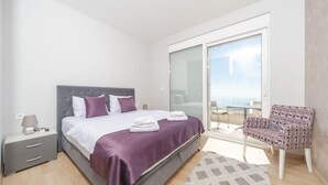 Un dormitorio moderno con cama, mesita de noche, silla y balcón con vistas.