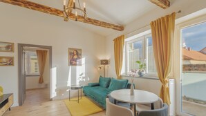 Un salon moderne avec un canapé vert, une table à manger avec des chaises, un tapis jaune et une grande fenêtre avec des rideaux.