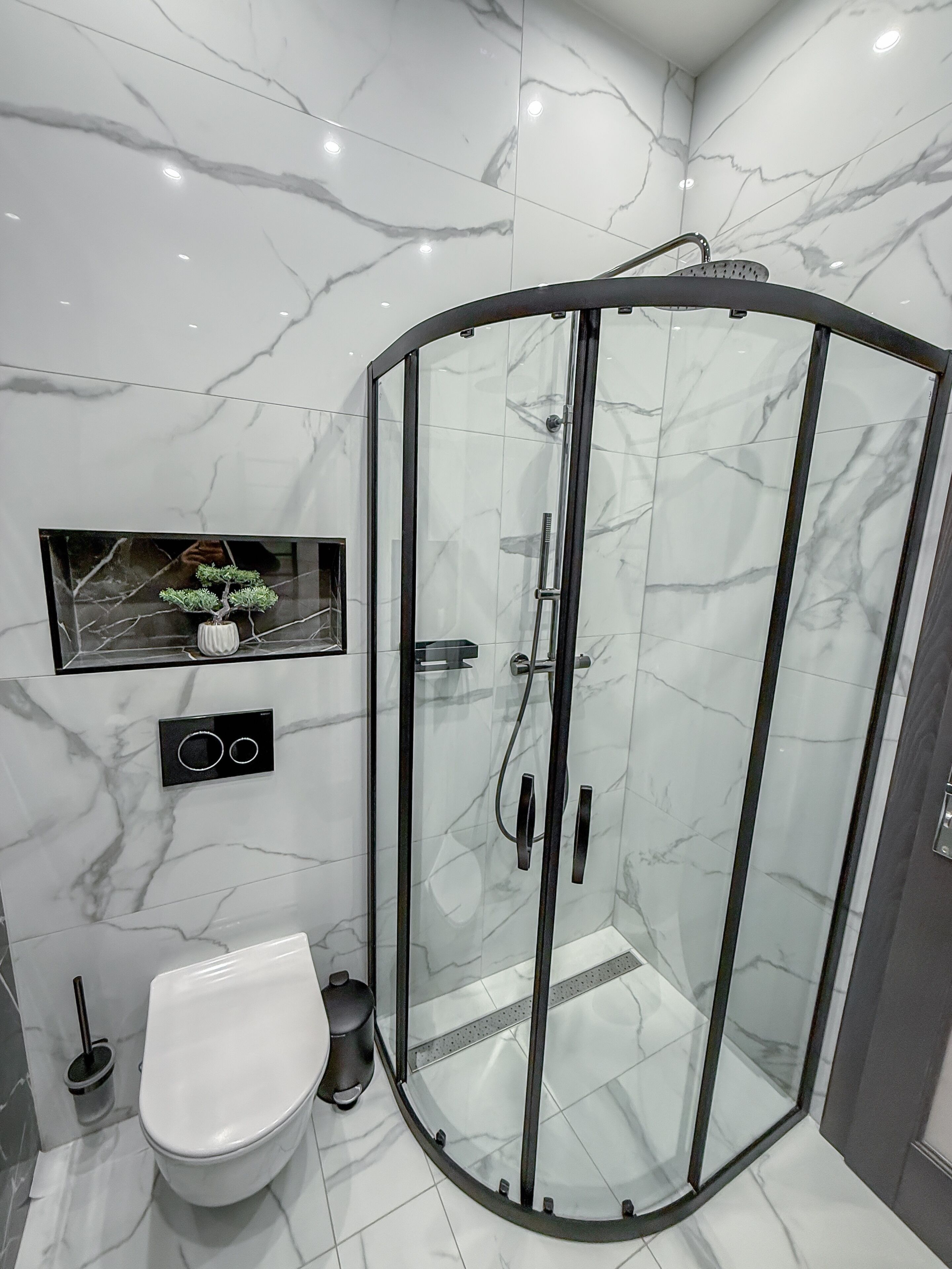 Une salle de bain moderne dotée d’une douche à parois de verre, de toilettes et d’un panneau de commande fixé au mur.