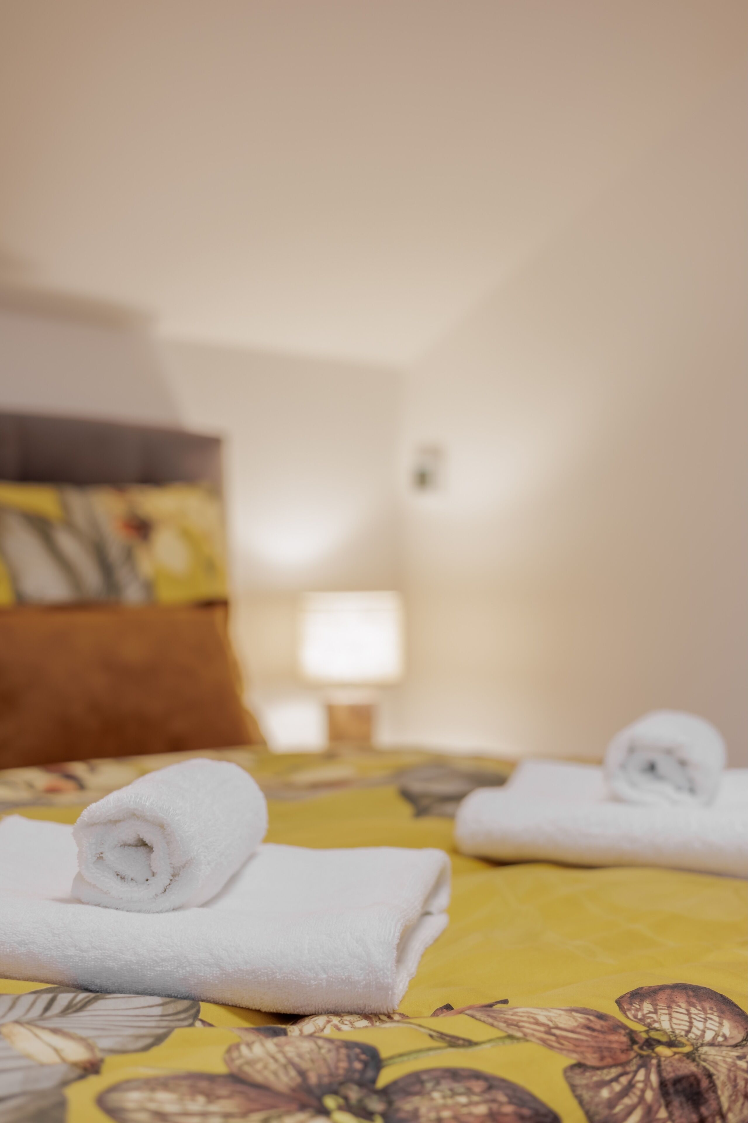 Ein Hotelzimmer mit einem Bett, einem Kopfkissen, einem zusammengerollten Handtuch und einer Lampe.