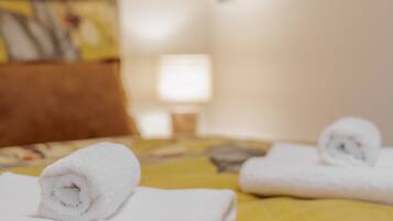 Ein Hotelzimmer mit einem Bett, einem Kopfkissen, einem zusammengerollten Handtuch und einer Lampe.