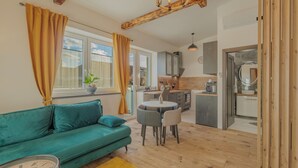 Un salon moderne comprenant un canapé, une table à manger et des chaises, un coin cuisine avec des placards et des appareils électroménagers, et une grande fenêtre avec des rideaux.