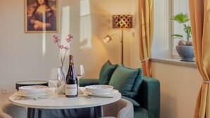 Une table à manger avec une bouteille de vin, des verres et un saladier, le tout placé devant un canapé vert et une fenêtre avec des rideaux.