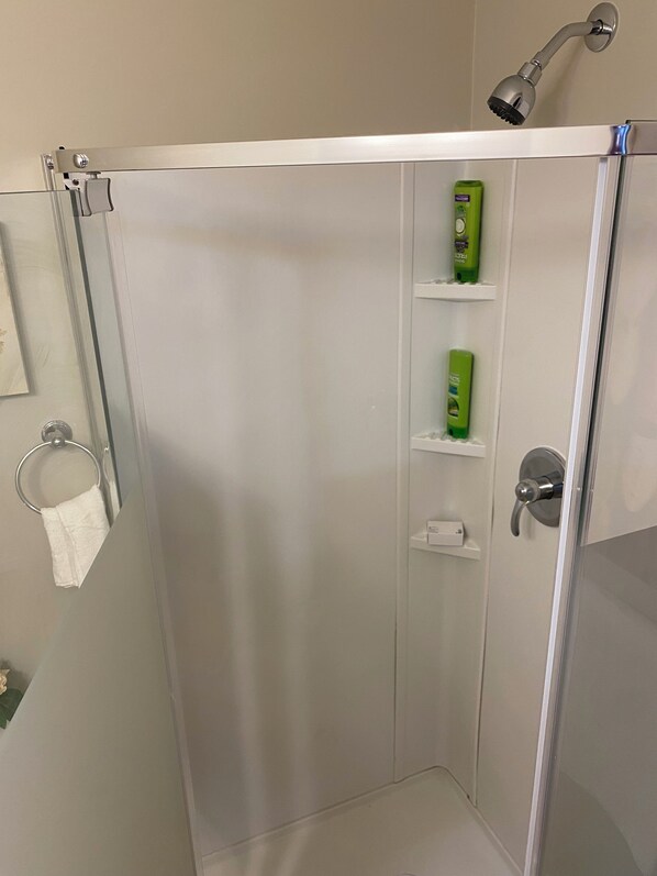 A shower with a glass door, a towel ring, and green toiletries on a shelf. - Cozy, Private Suite in Bedford — Bed, Laundry,kitchenette and Self Check in (Halifax)
