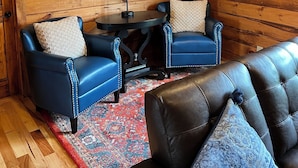L’intérieur d’un chalet accueillant, avec des murs en bois, deux canapés en cuir bleu, une table ronde et des têtes d’animaux fixées au mur.