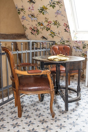 A dining area with a round table and two chairs, a decorative wall with floral patterns, and a tiled floor. - Maison Da Silva (Oberderdingen)