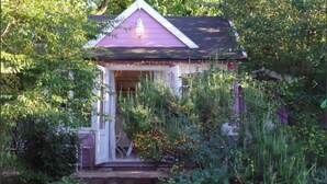 A small, single-story house with a purple exterior and a white door, surrounded by dense greenery. - Maison Da Silva (Oberderdingen)