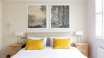 A bedroom with a large bed, two bedside tables with lamps, and two framed landscape paintings above the bed.