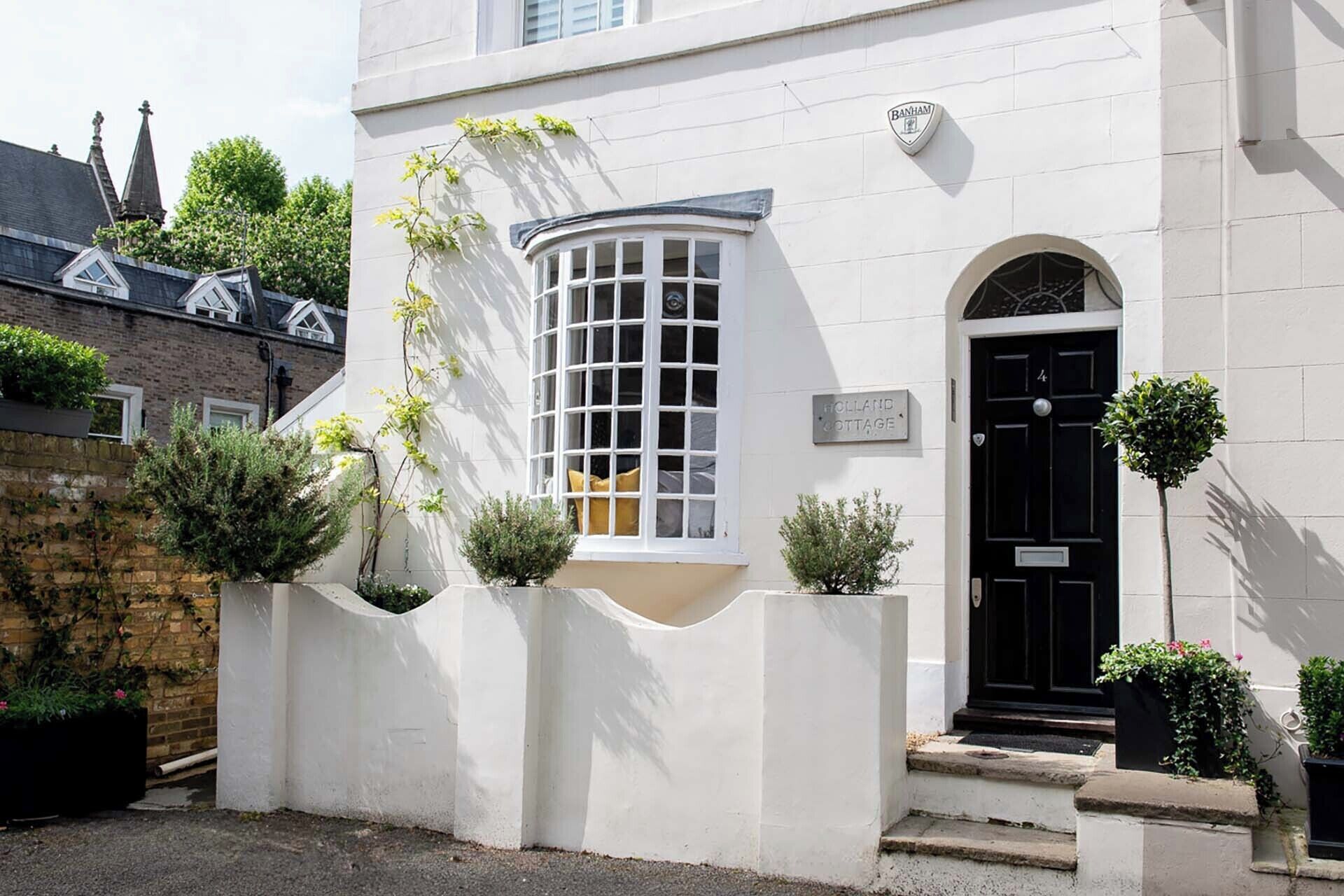 A white building with a black door, a window with a grid pattern, and a sign that reads "HOLLAND COTTAGE."