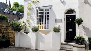 Un edificio blanco con una puerta negra, una ventana de diseño cuadriculado y un letrero que dice "HOLLAND COTTAGE".