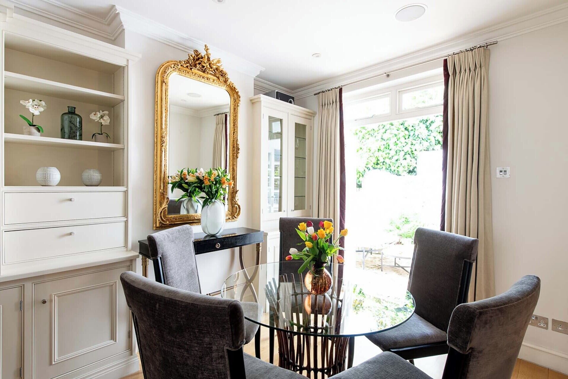 A room with a dining table, two chairs, a mirror, and a view of the outdoors.