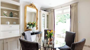 A room with a dining table, two chairs, a mirror, and a view of the outdoors.