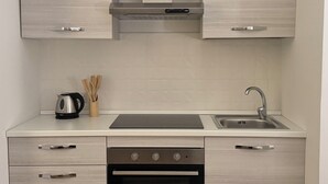 Una cucina moderna con mobili chiari in legno, una cappa in acciaio inossidabile, forno integrato, lavello e bollitore sul piano di lavoro.