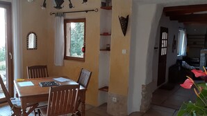 A dining area with a wooden table and chairs, a window with curtains, and a view of greenery outside. - Character house Luberon, nature, swimming pool (Saint-Saturnin-lès-Apt)